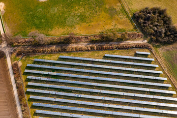 Photovoltaic modules of a solar farm bordering a dirt road and agricultural fields from a drone's...