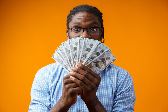 Portrait of amazed young man in casual shirt holding dollar banknotes against yellow background