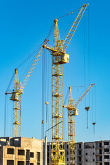 Three high construction tower cranes against the blue sky. Construction of a multi-storey building.