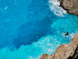 Top view of bright blue turquoise sea waters with grey rocks. Storm waves crash against the rocks near shipwreck beach Zakynthos Greece.