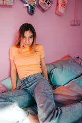 Portrait of young attractive cheerful woman sitting in a bedroom with pink walls .