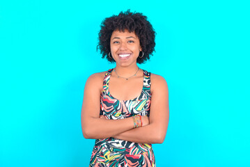 young woman with afro hairstyle in sportswear against blue background being happy smiling and crossed arms looking confident at the camera. Positive and confident person.