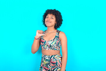 Closeup of cheerful young woman with afro hairstyle in sportswear against blue background looks...