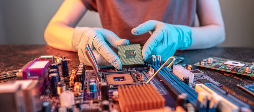 Engineer's gloved hand is holding the CPU chip on the background of the motherboard. High-tech hardware microelectronics