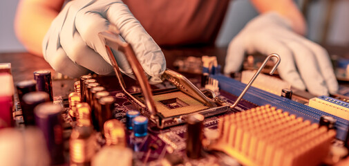 Engineer's gloved hand is holding the CPU chip on the background of the motherboard. High-tech hardware microelectronics
