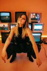 Portrait of young attractive caucasian woman in stylish outfit posing near stand with retro tvs.