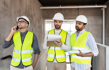 architecture, construction business and people concept - male architects in helmets with smartphone, blueprint and clipboard working at office building