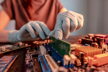The engineer's gloved hand holds the computer's RAM chip against the background of the motherboard
