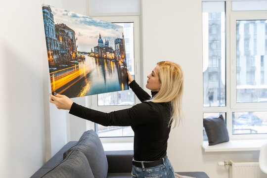 Canvas print with gallery wrap. Woman hangs photography on white wall. Hands holding photo canvas print.