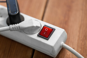 electricity, energy and power consumption concept - close up of socket with plugs, charger and red switch button on wooden floor