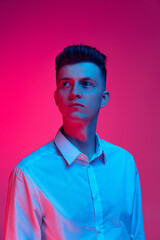 Obraz premium Half-length portrait of young handsome man in white shirt posing isolated over magenta color studio background in blue neon light