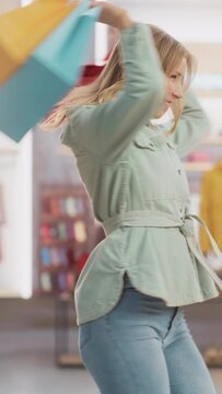 Vertical Footage of an Young Woman at Clothing Store Counter Taking Shopping Bags with Clothes from Friendly Retail Sales Assistant, Goes Away in Happy Mood, Smiling, Spinning and Dancing.