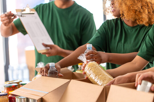 charity, donation and volunteering concept - close up of international group of happy smiling volunteers packing food in boxes at distribution or refugee assistance center