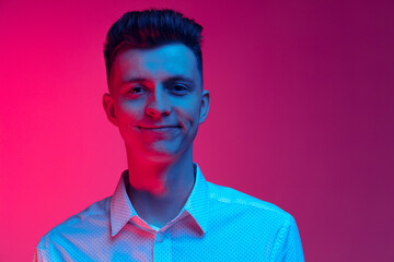 Young happy man in white shirt smiling isolated over magenta color studio background in blue neon light. Concept of positive emotions