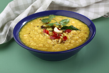 Indian food tuvar Daal or yellow lentil soup or curry in blue ceramic bowl on green background
