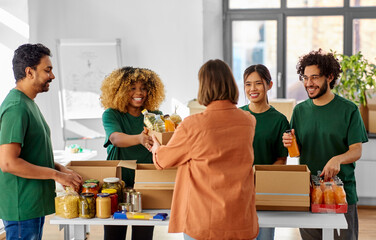 charity, donation and volunteering concept - happy smiling male volunteer with clipboard and woman taking box of food at distribution or refugee assistance center