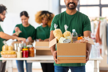 charity, donation and volunteering concept - happy smiling male volunteer with food in box and...