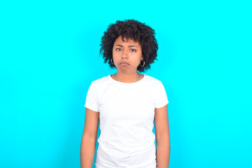 young woman with afro hairstyle wearing white T-shirt against blue wall depressed and worry for distress, crying angry and afraid. Sad expression.