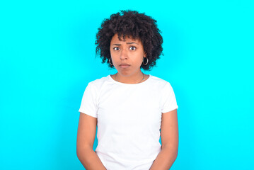 young woman with afro hairstyle wearing white T-shirt against blue wall Pointing down with fingers showing advertisement, surprised face and open mouth