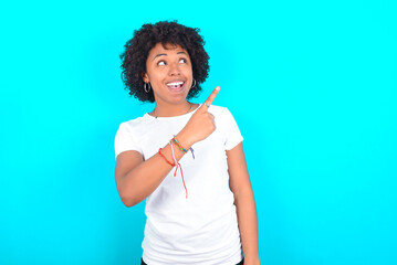 young woman with afro hairstyle wearing white T-shirt against blue wall glad cheery demonstrating copy space look novelty