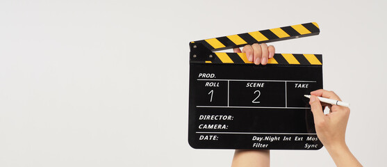The hand is holding a yellow and black clapper board and a marker Pen with a written number on the...