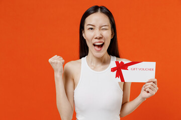 Young woman of Asian ethnicity 20s in white tank top hold gift certificate coupon voucher card for...