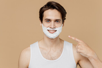 Attractive smiling young man 20s perfect skin in undershirt point finger on face covered with...