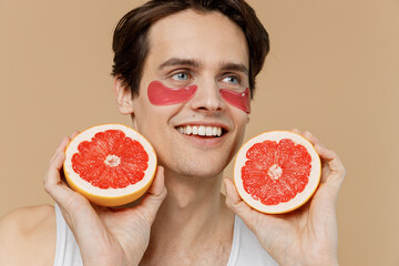 Young fun man 20s perfect skin in undershirt wear gold patch under eye hold half of grapefruit look...