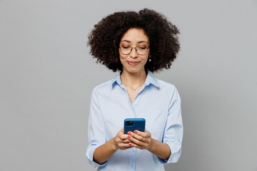 Young smiling employee business corporate lawyer woman of African American ethnicity in classic formal shirt work in office hold in hand use mobile cell phone isolated on grey color background studio.