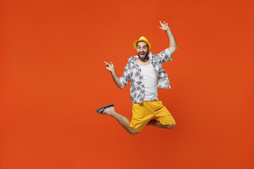 Full body winner excited exultant jubilant young tourist man in beach shirt hat jump high raise up hands isolated on plain orange background studio portrait Summer vacation sea rest sun tan concept.