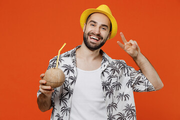 Young happy fun tourist man in beach shirt hat hold cocktail juice in coconut bowl with straw show...