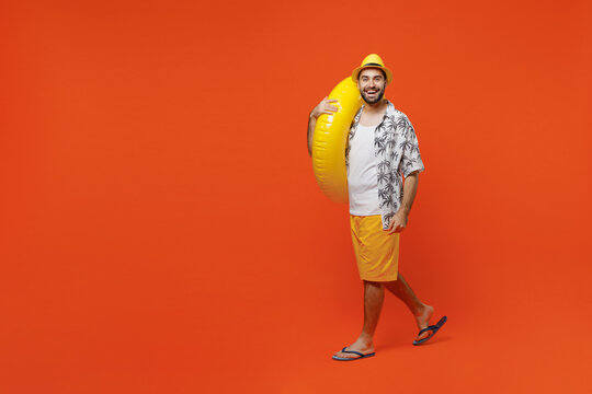 Full body young happy fun cool tourist man wear beach shirt walking going strolling hold inflatable ring isolated on plain orange background studio portrait. Summer vacation sea rest sun tan concept.