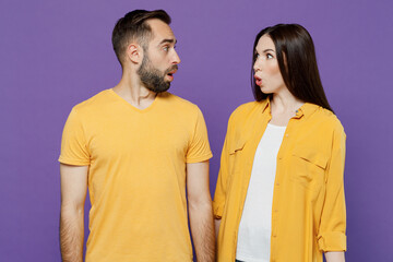 Young shocked surprised couple two friends family amazed man woman 20s together wearing yellow casual clothes look to each other with opened mouth isolated on plain violet background studio portrait.