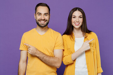 Obraz premium Young smiling happy couple two friends family man woman together in yellow casual clothes looking camera point index finger aside on workspace area isolated on plain violet background studio portrait.