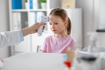 Obraz na płótnie Canvas medicine, healthcare and pediatry concept - female doctor or pediatrician measuring little girl patient's temperature with infrared forehead thermometer at clinic