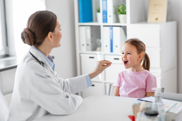 Obraz premium medicine, healthcare and pediatry concept - female doctor or pediatrician with tongue depressor checking little girl patient's throat on medical exam at clinic