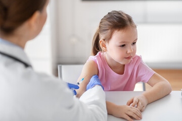 Fototapeta premium medicine, healthcare and vaccination concept - female doctor or pediatrician with syringe making vaccine injection to little girl patient at clinic