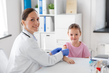 medicine, healthcare and vaccination concept - female doctor or pediatrician talking to little girl...