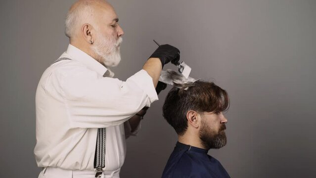 Hairdresser is dying male hair. Coloring man hair process. Man dyeing hair while using a brush. Colouring of gray hair at barber salon. Haircare and men hairstyling.