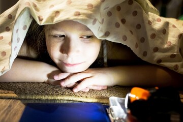 Cute little girl hides under a blanket and reads a fairy tale about a magical space world