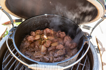 outdoor cooking - goulash from venison meat in a dutch oven on a charcoal grill at a sunny day
