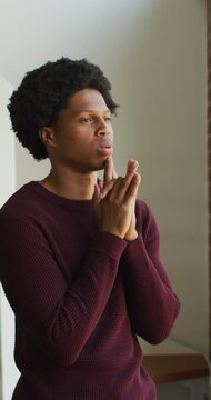Vertical video of thoughtful african american man looking out of window, with hands clasped