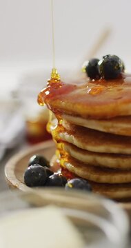 Vertical video of maple syrup pouring on stack of american style pancakes topped with blueberries
