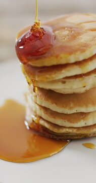 Vertical video of maple syrup pouring onto stack of american style pancakes