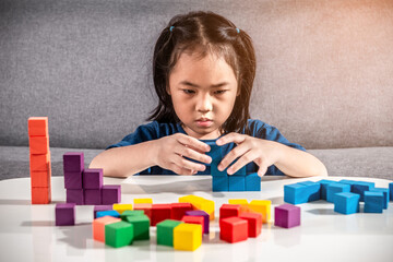 Asian girl plays with small wooden colorful toy blocks at home or kindergarten. A Girl enjoys playing with construction blocks for toddler kids. Education Development Construction creative toys Idea