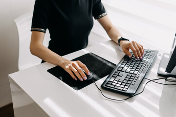 Closeup of a woman working at a computer, holding a mouse on mouse pad and typing on keyboard.