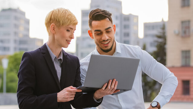 Serious diverse multiracial couple colleagues arabic hispanic man and caucasian woman standing near business center at street outdoors and working on laptop discuss project analyze data teamwork - Powered by Adobe