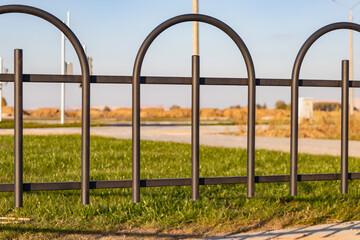 Fototapeta premium A metal fence between the roadway and the sidewalk. An empty pedestrian path with a fence. Multi-lane road with a pedestrian path next to it separated by a railing.