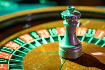 Roulette wheel in a casino with green light shining over the table 