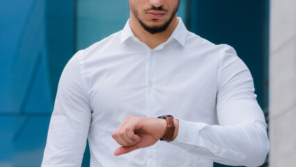 Unrecognizable arabic Hispanic business man with beard young boss leader manager wears white formal shirt looks at wrist watch angry of late time lateness checks hour waving head no negative upset - obrazy, fototapety, plakaty